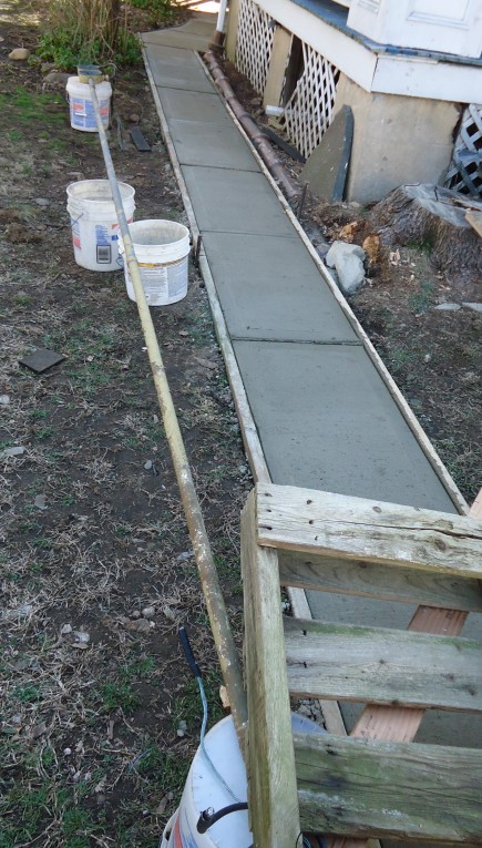 Fresh concrete being finished beside a house.
